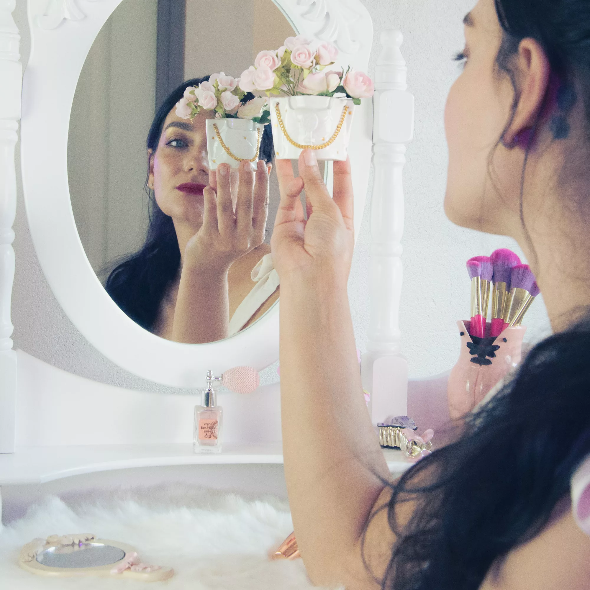 Femme tenant un mini pot en porcelaine blanche orné de fleurs, en face d'un miroir