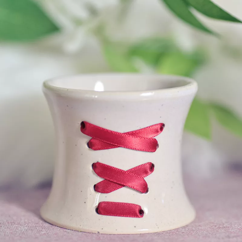 Petit pot en céramique orné d'un lacet de satin rouge, rappelant les corsets des femmes d'époque (lacet rouge)